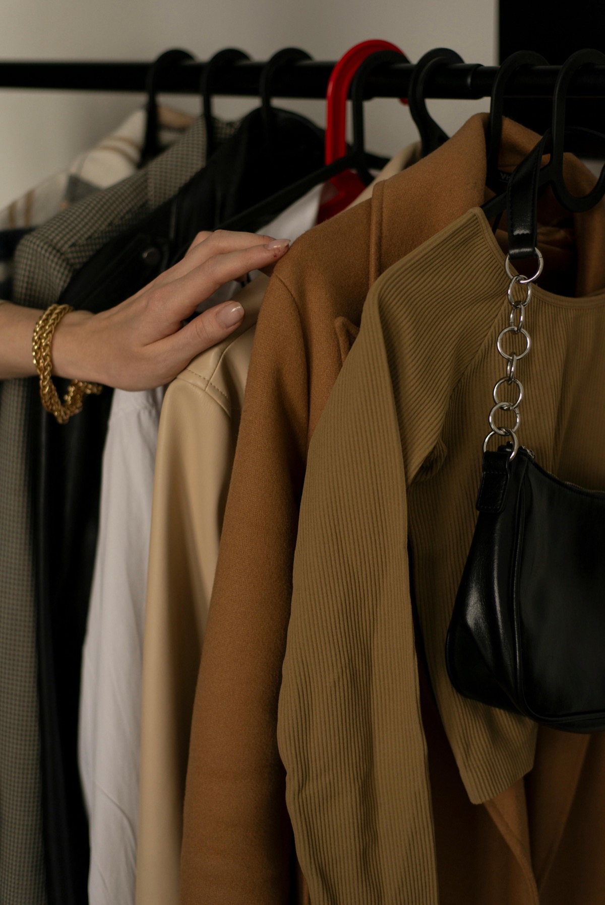 Main qui parcourt une tringle de vestes et de sacs
